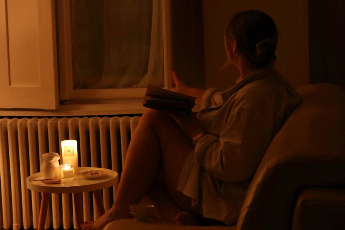 Mujer en bata leyendo un libro a la luz de las velas con una taza de té, una rutina de transición tranquila antes de dormir