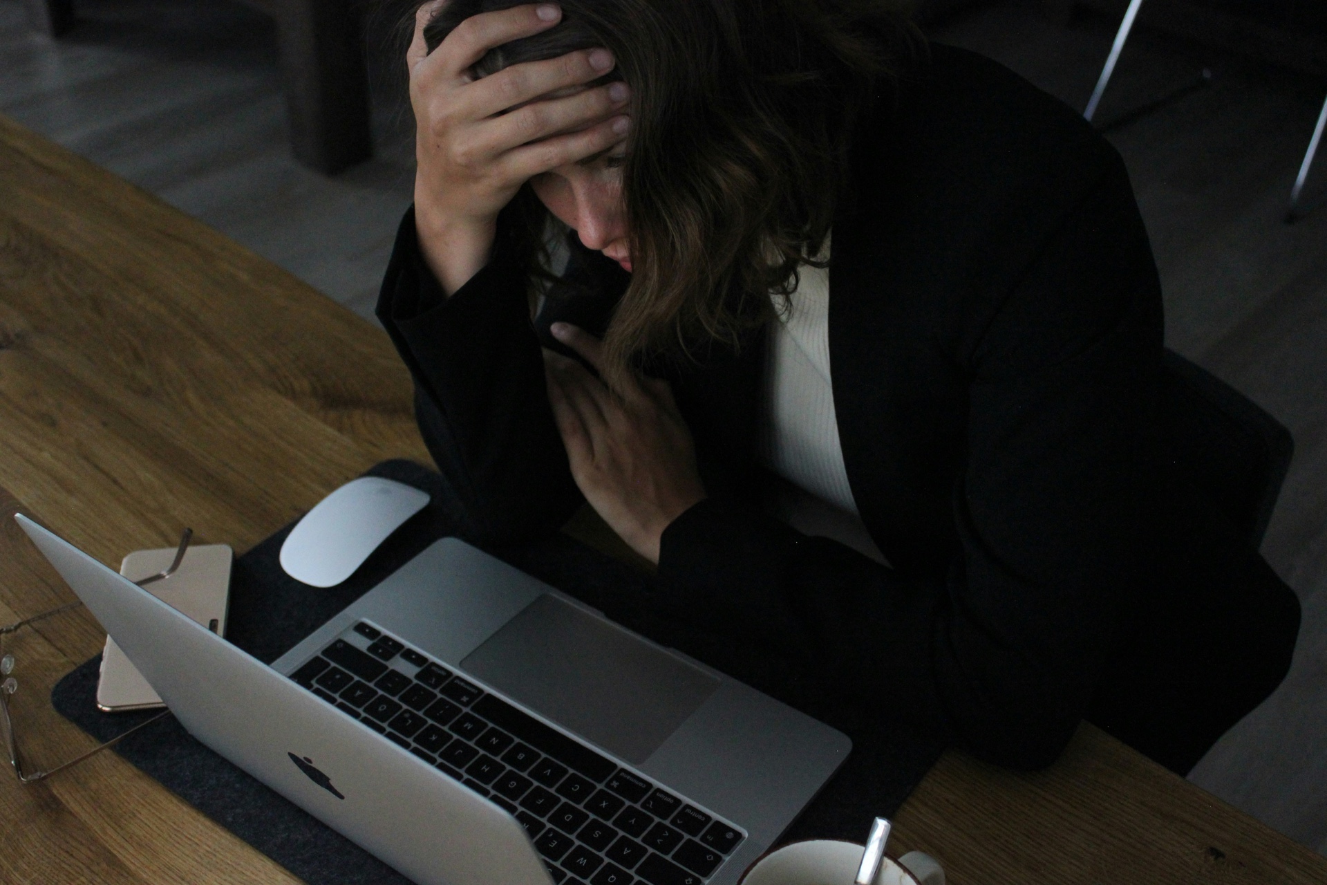 Mujer inclinada frente a una computadora con una mano sobre la frente, abrumada por el estrés laboral crónico