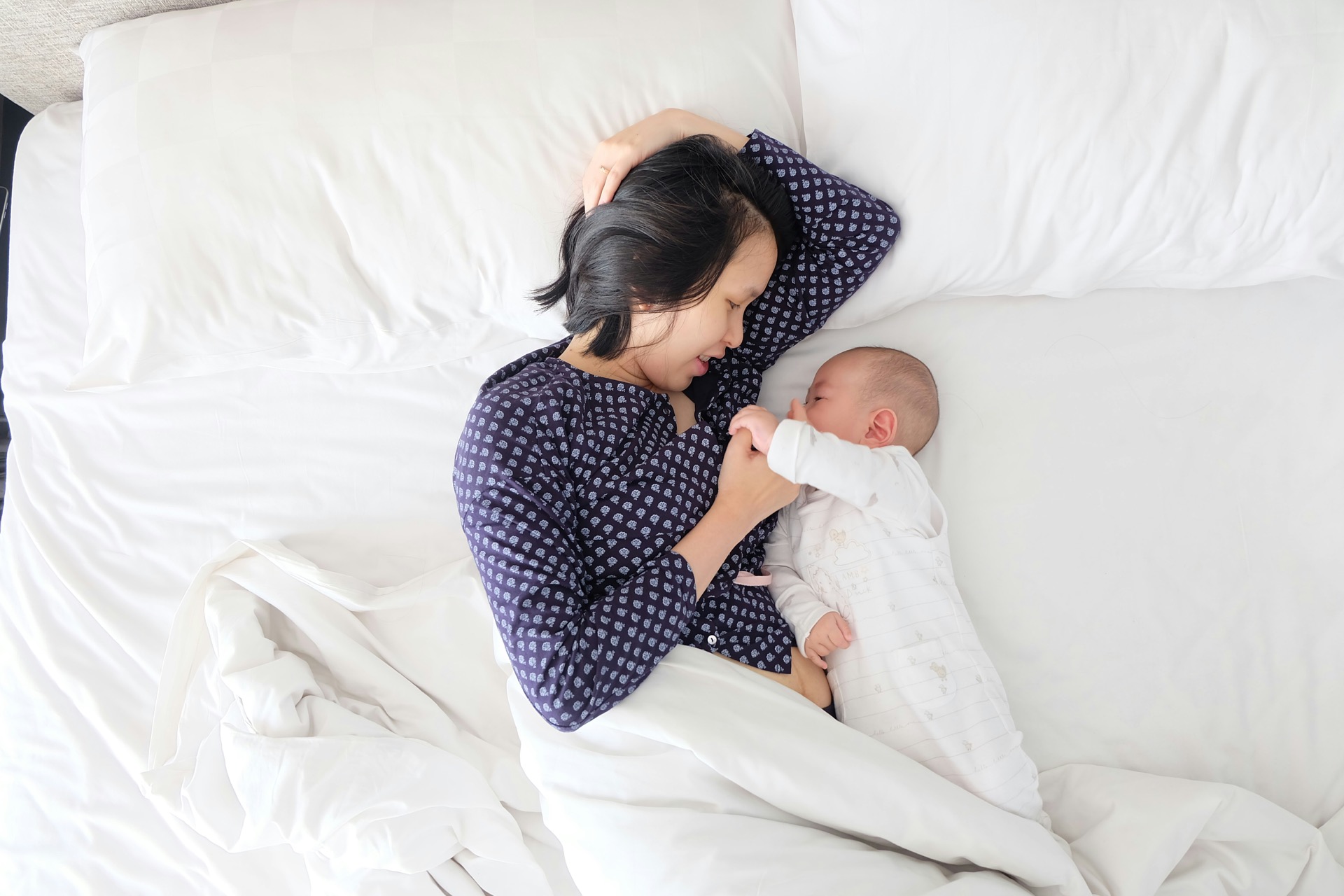 A parent lying beside their baby and holding their hand