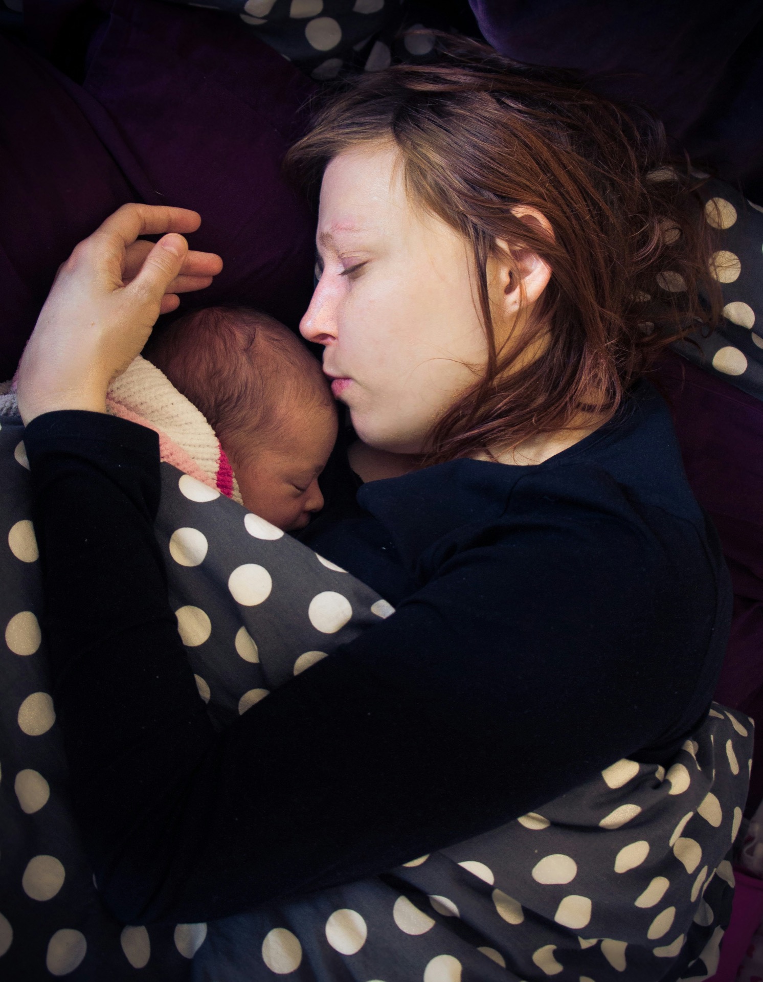 A parent with eyes closed holding a baby close to their chest