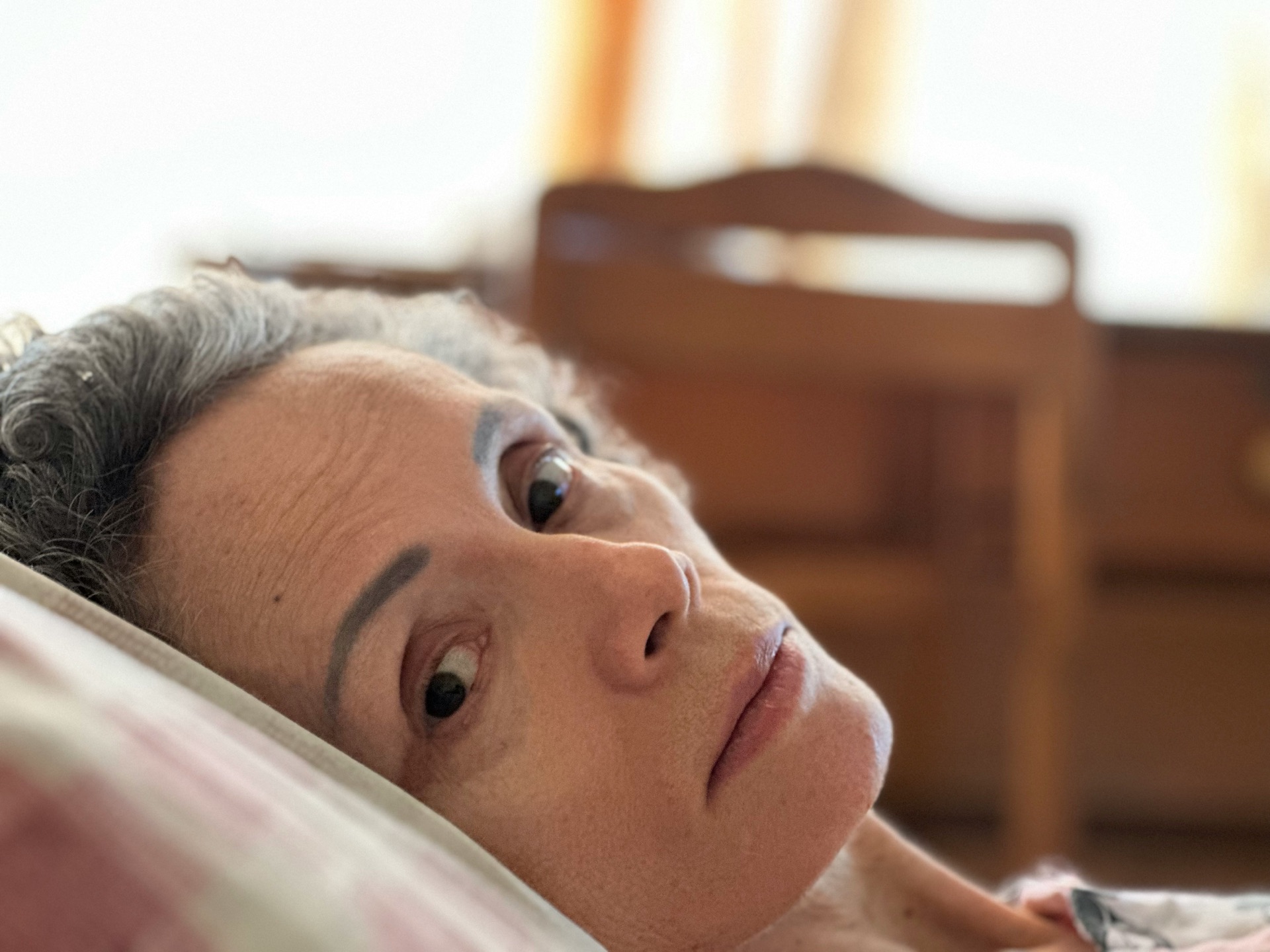 Una persona mayor acostada con los ojos abiertos y la cabeza sobre una almohada