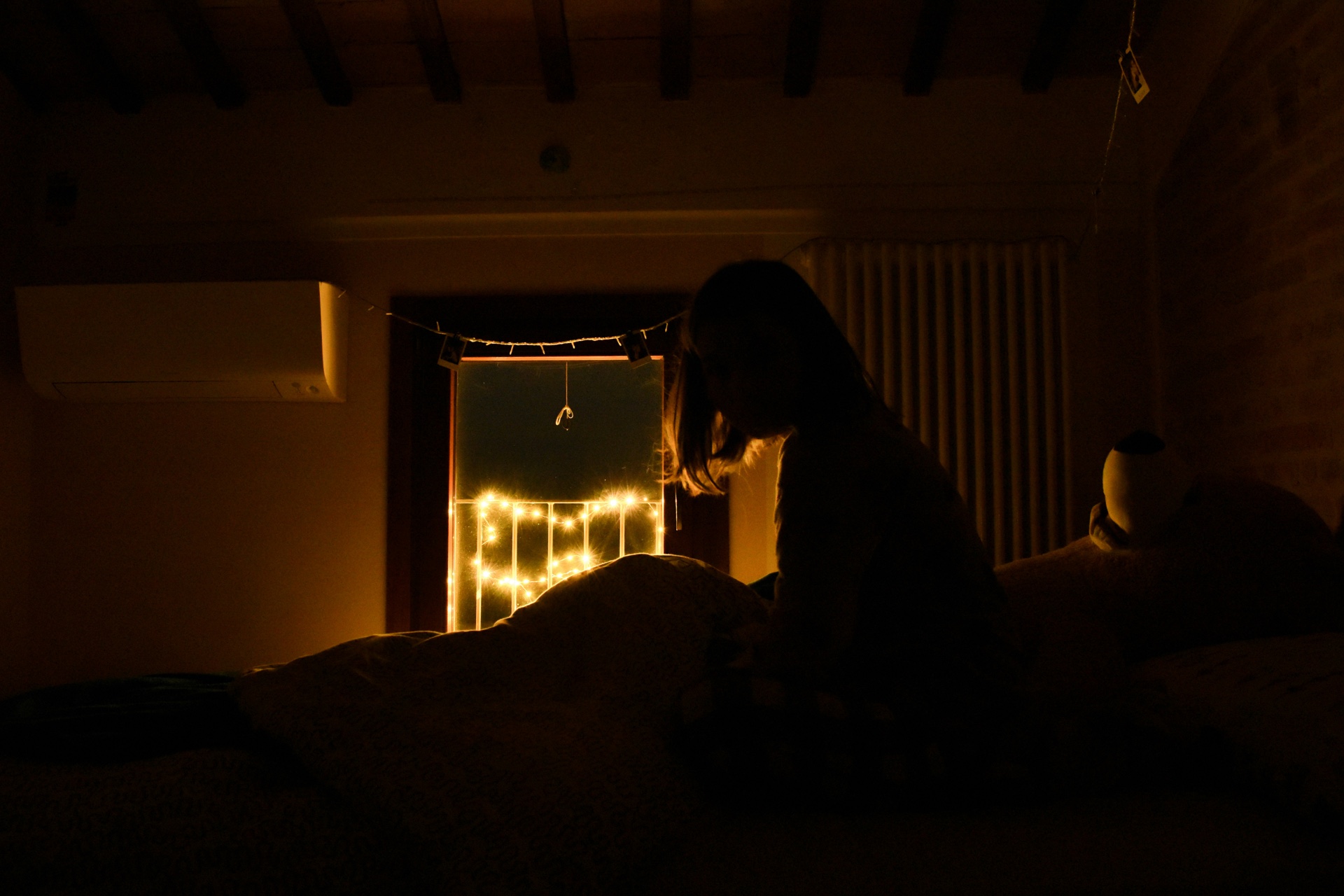 Silueta de una mujer sentada y despierta en la cama durante la noche, con luces cálidas al otro lado de la ventana