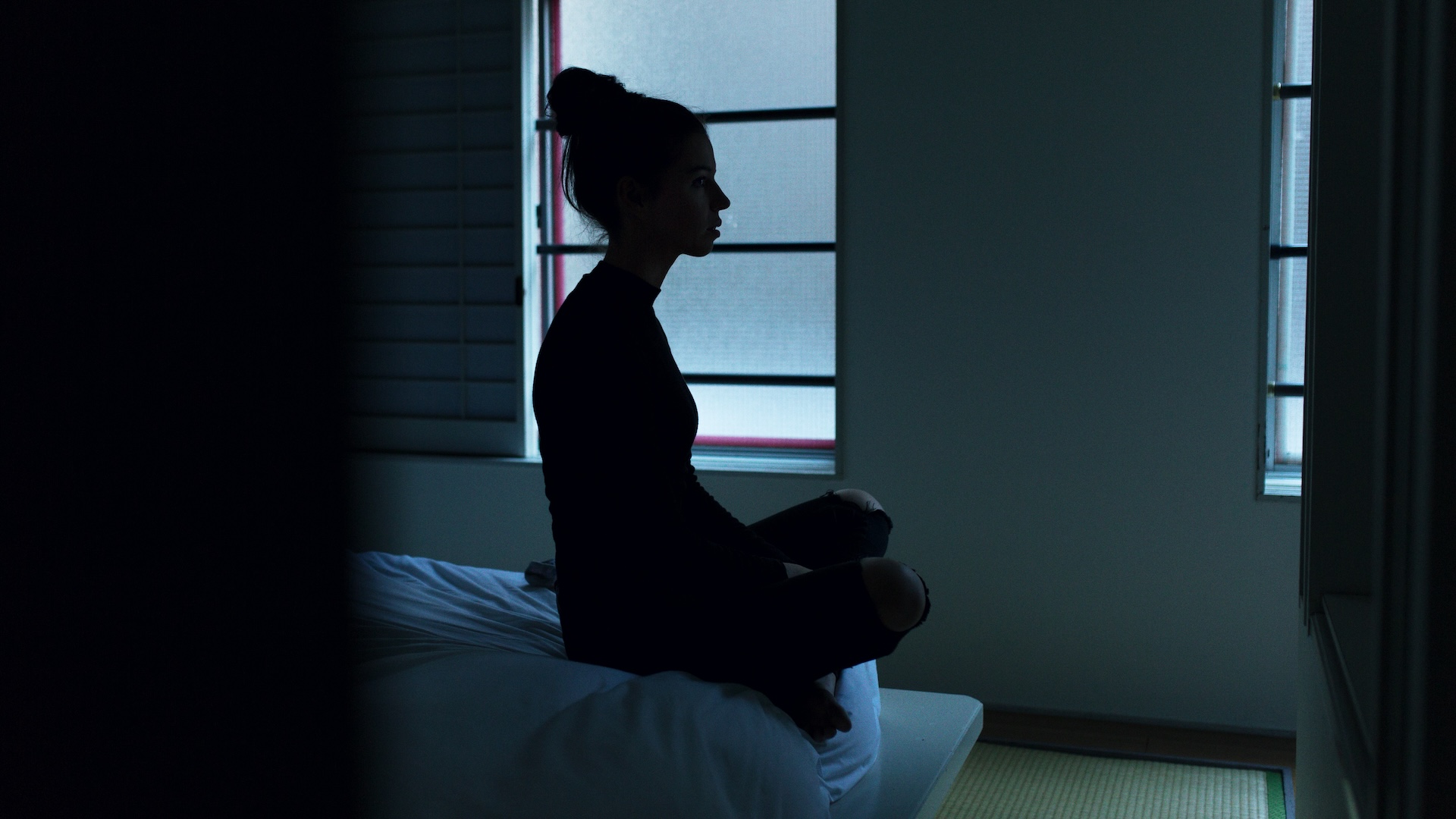 Mujer sentada con las piernas cruzadas en su cama de noche, completamente despierta y mirando hacia la ventana