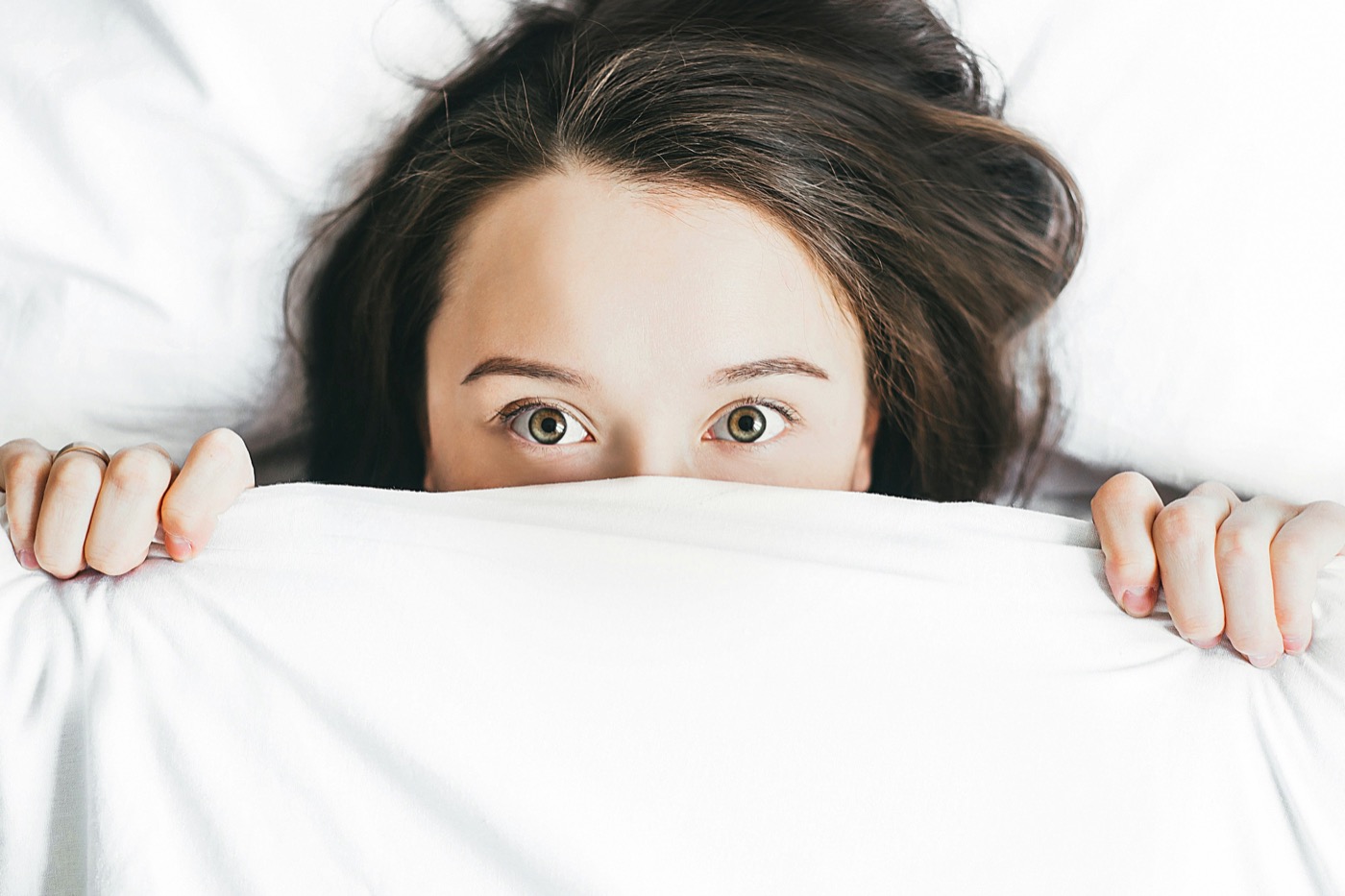 Mujer acostada en la cama de noche tapándose la cara con el edredón, con los ojos bien abiertos y sin poder dormir